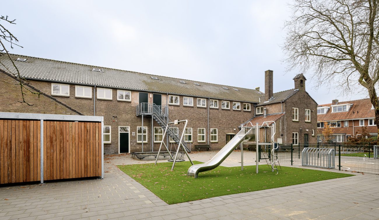 Binnenplaats basisschool met kunstgras, schommels, glijbaan en fietsenrek – Cartesius, Utrecht