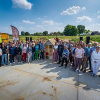 Grote groep mensen verzameld buiten op een open terrein onder een blauwe lucht.