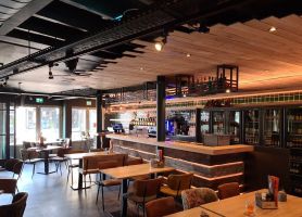 Warm eetcafé-interieur met houten bar, tapkranen en tafels met leren stoelen onder een houten plafond.