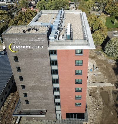 Bastion Hotel Geleen – luchtfoto van dak met installaties, logo op zijgevel en rood-bakstenen kopgevel, terrein in aanleg