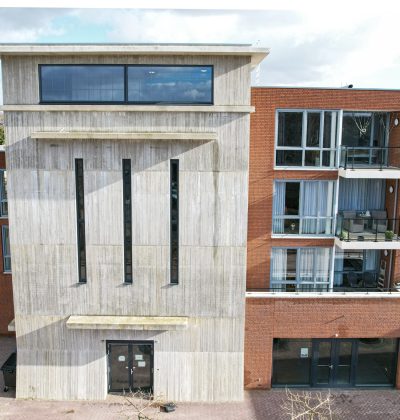 MFA Hart voor Treebeek Brunssum – betonnen torenvolume met smalle verticale ramen naast bakstenen gevel met glazen balkons