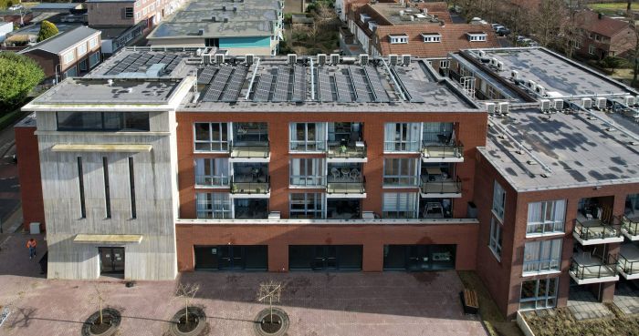 MFA Hart voor Treebeek Brunssum – frontgevel met betonnen toren links, bakstenen blok met glazen balkons en plat dak met zonnepanelen boven stadsplein