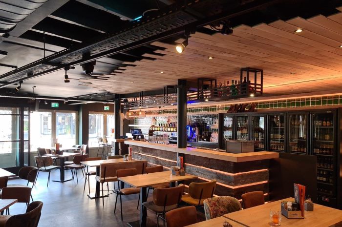 Warm eetcafé-interieur met houten bar, tapkranen en tafels met leren stoelen onder een houten plafond.