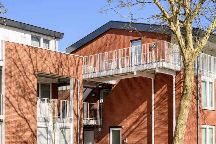 Renovatie Plataanlaan Baarn: rode baksteen witte galerijen en loopbrug en nieuwe gevels en kozijnen.