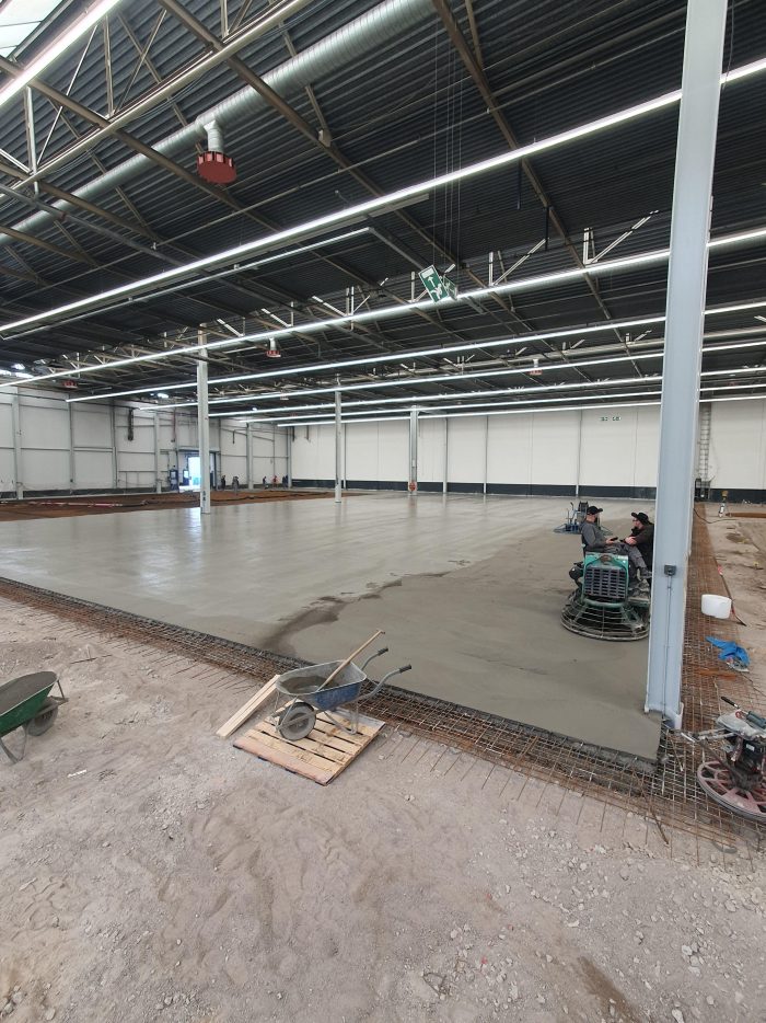 Giet- en afwerkfase van de nieuwe betonvloer in hal A50 bij DAF Eindhoven, met vlindermachines die de verse betonplaat afwerken in de fabriekshal.