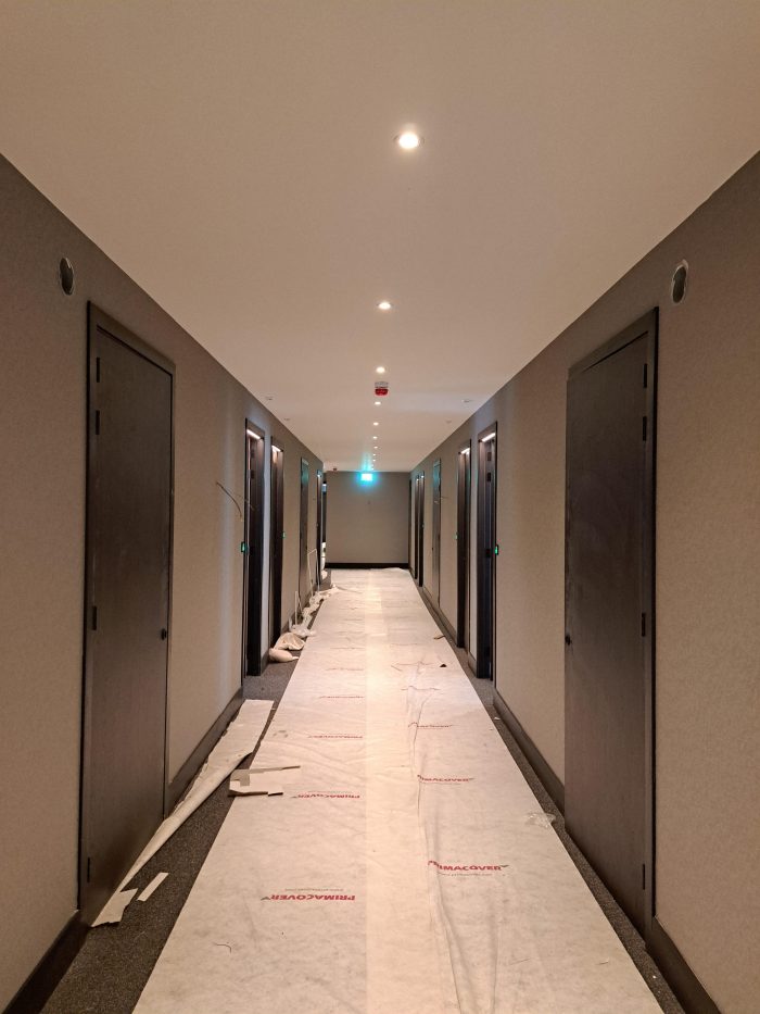 Uitbreiding en renovatie Van der Valk Hotel Wassenaar – hotelgang in afbouw met schilderklare wanden, nieuwe deuren en beschermfolie over de vloer, spotverlichting aan het plafond.