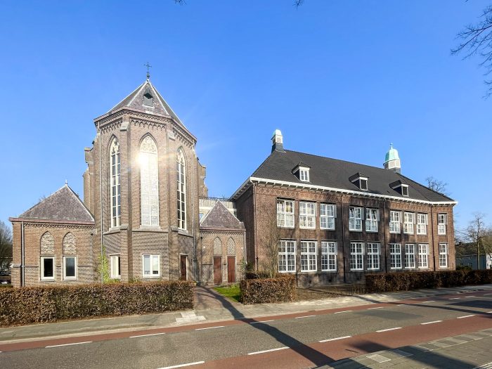 Verbouwing Huize Padua Boekel – straataanzicht van het monumentale complex met kapel en gotische ramen, bakstenen gevels en witte kozijnen onder een heldere blauwe lucht.
