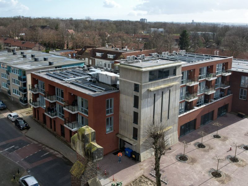 MFA Hart voor Treebeek Brunssum – luchtfoto van bakstenen complex met betonnen toren, balkons en plat dak met installaties aan plein met bomen