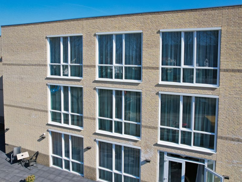 Gevel van een modern bakstenen gebouw met grote ramen over meerdere verdiepingen.