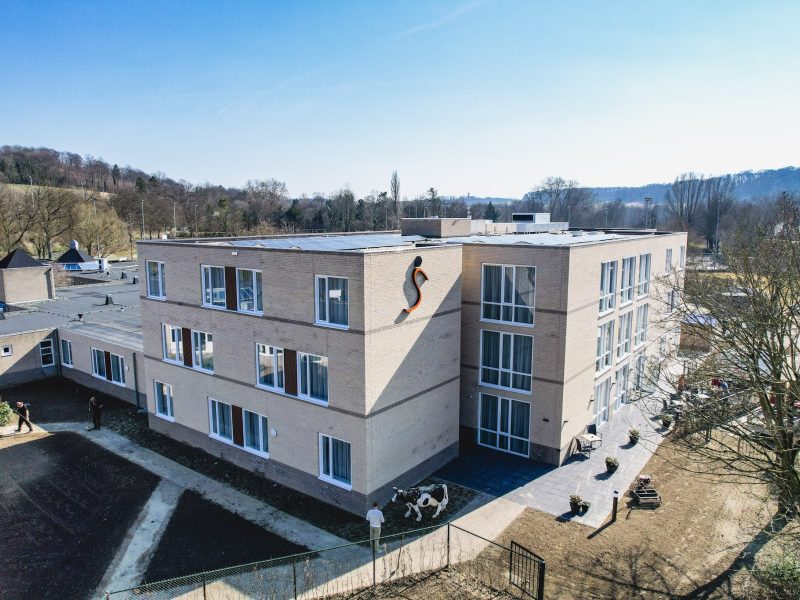 Modern gebouw met meerdere verdiepingen, grote ramen en een fiets bij de ingang, omgeven door bomen.