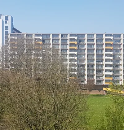 Appartementencomplex met gestapelde balkons achter bomen en groen grasveld